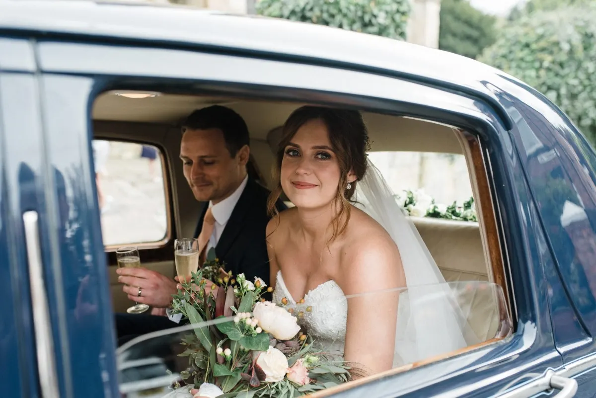 Bride and groom sharing a toast in the back of a vintage car