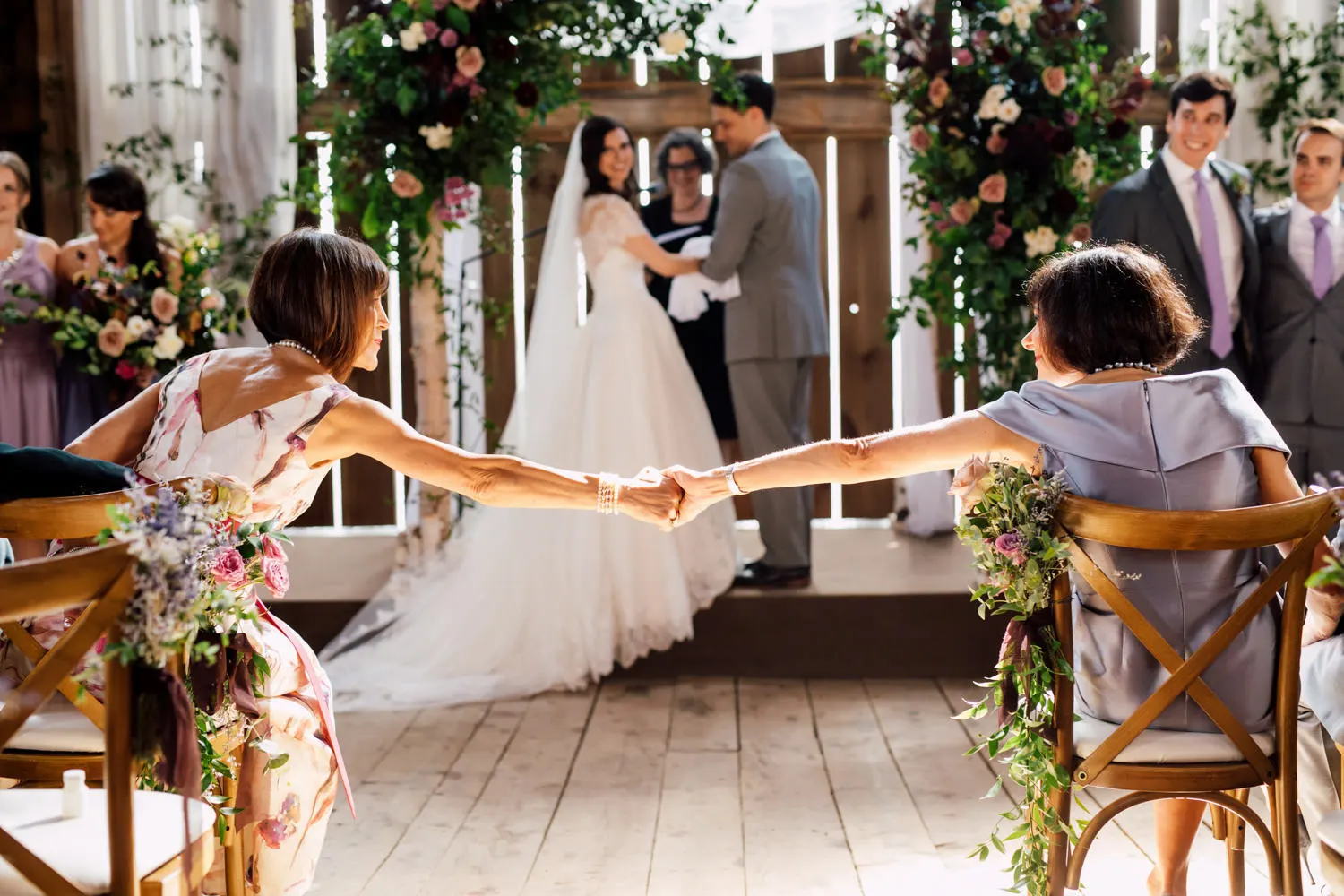 Bride and groom exchanging vows as their mothers hold hands across the aisle
